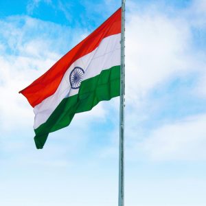 The Indian national flag waving proudly on a flagpole against a bright, clear blue sky.